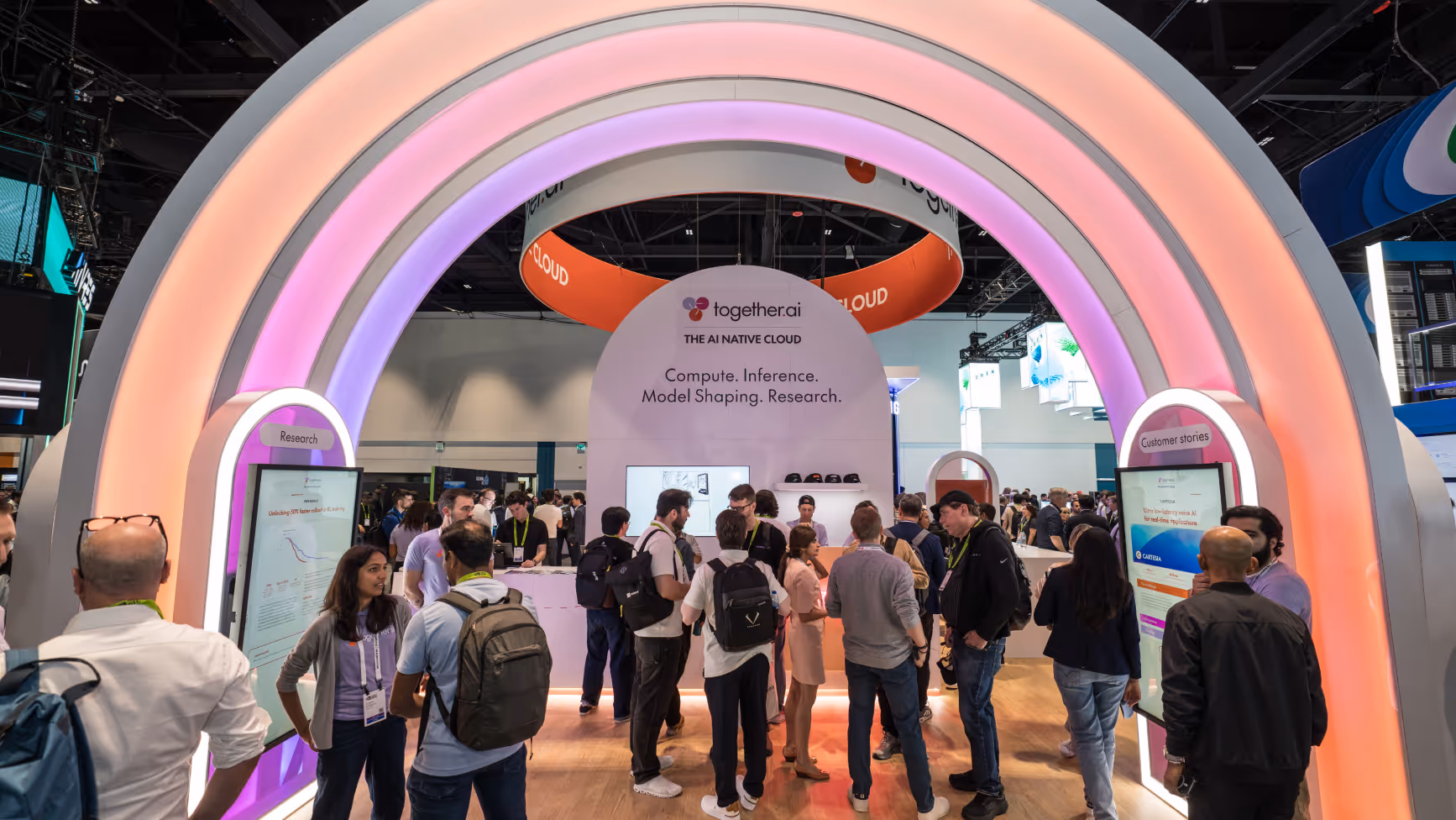 Crowd of people gathered at the together.ai booth with colorful illuminated arches and signage about AI cloud computing, inference, model shaping, and research.