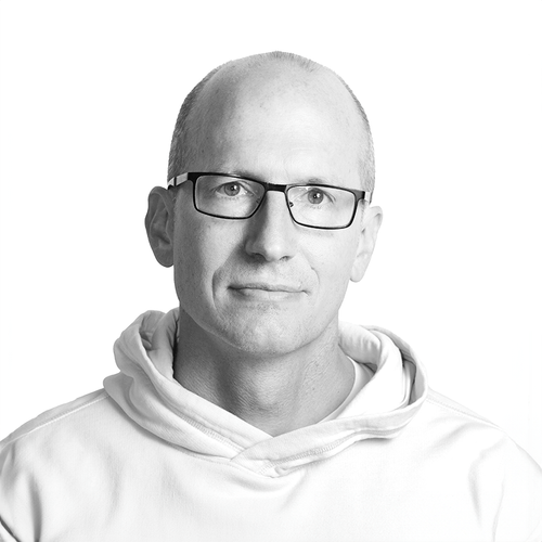 Portrait of a middle-aged man with glasses wearing a light hooded sweatshirt against white background.