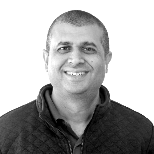Smiling man with short hair wearing a quilted jacket over a collared shirt on white background.