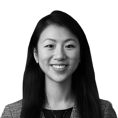 Smiling young woman with long dark hair wearing a blazer and necklace in a black and white photo.