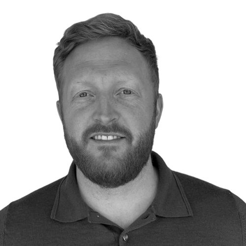 Smiling man with short hair and beard wearing a dark buttoned polo shirt against a white background.