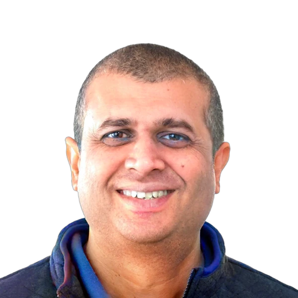 Smiling man with short hair wearing a quilted jacket over a collared shirt on white background.