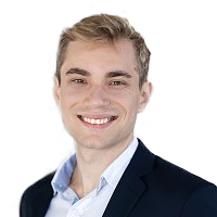 Smiling man with short blond hair wearing a navy blazer and light blue shirt against a white background.