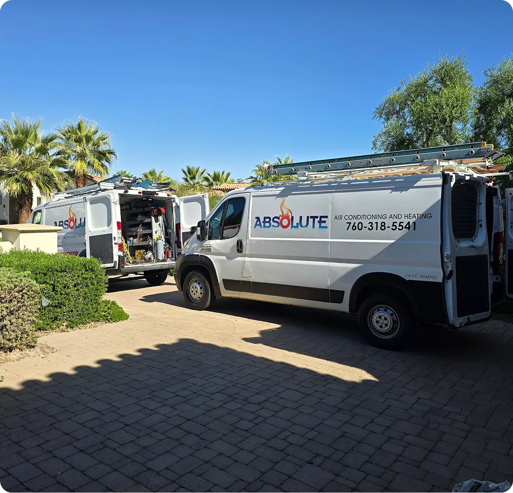 Two white vans with ladders on top parked on a driveway, one with open rear doors showing HVAC equipment, both branded with Absolute Air Conditioning and Heating and phone number 760-318-5541.