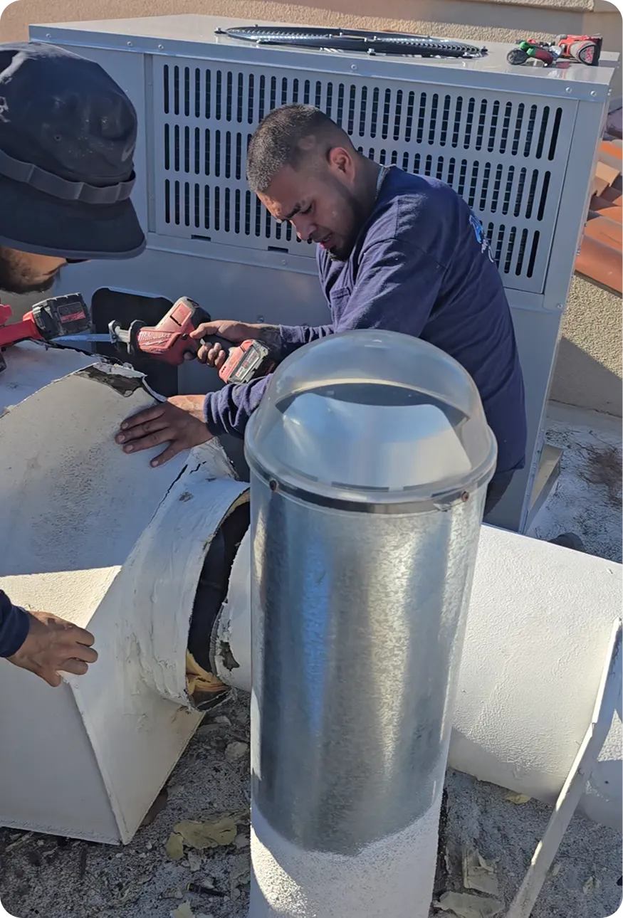 Two men working on HVAC ducting outdoors using a power drill near a large air conditioning unit.