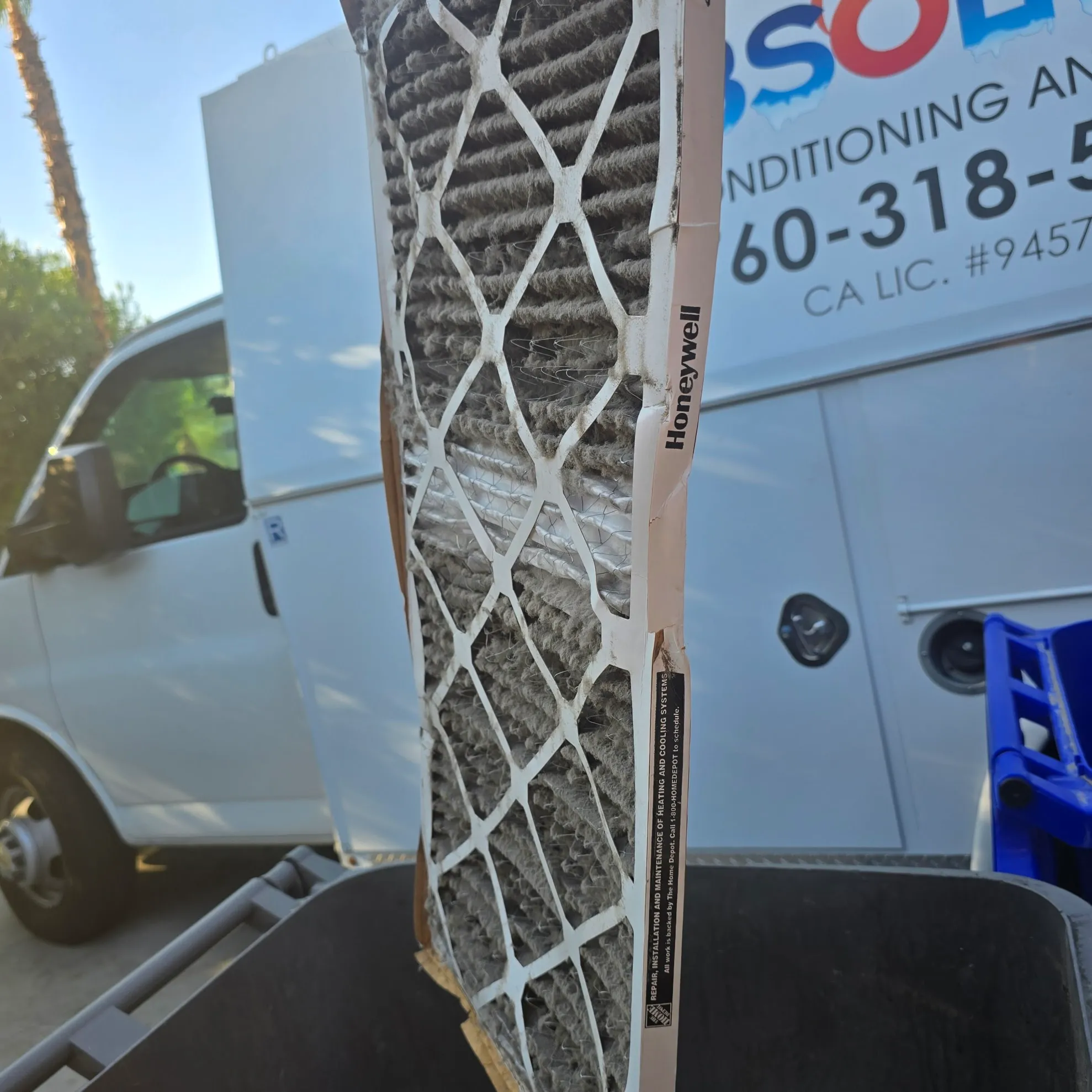Close-up of a dirty Honeywell air filter held in front of a white service van.