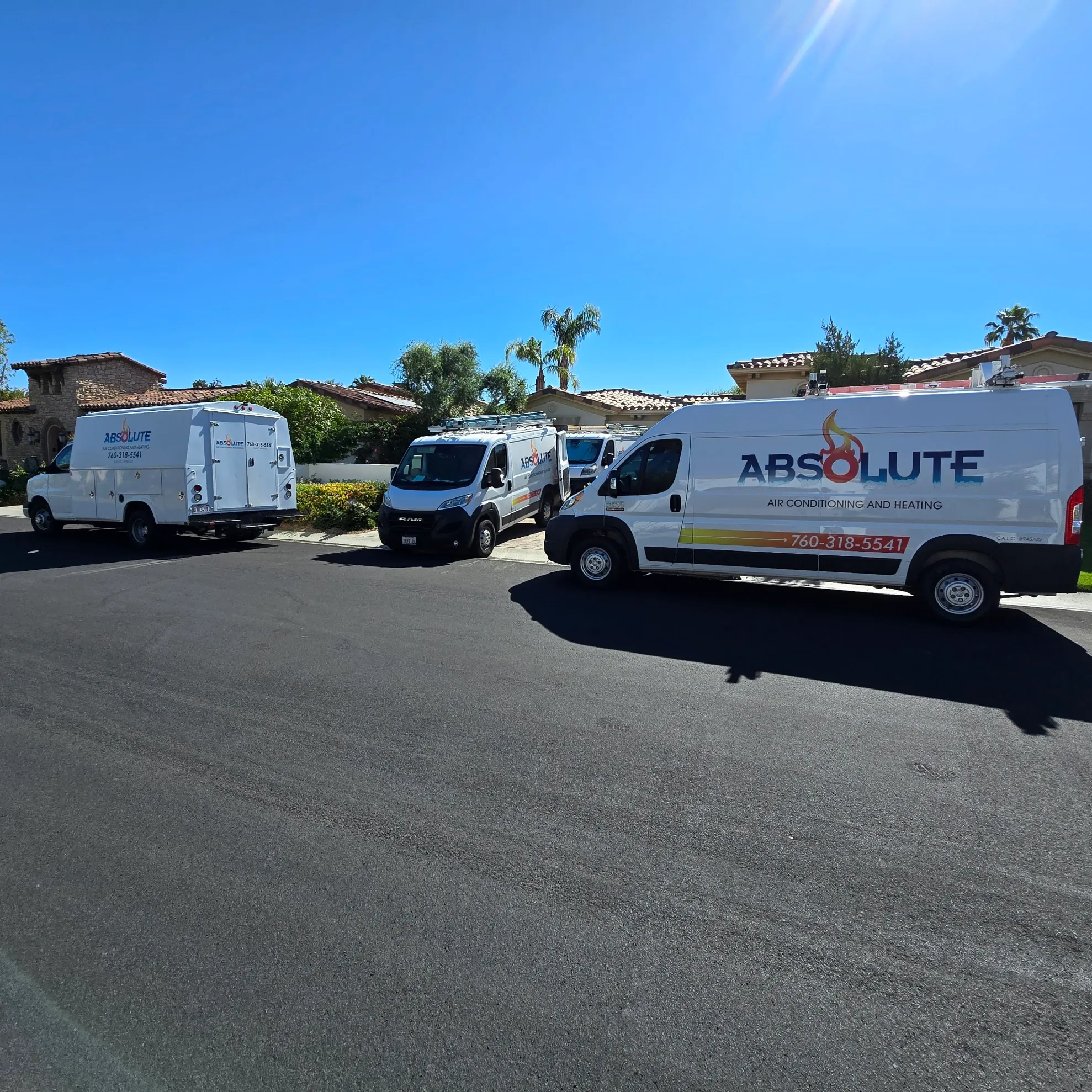 Three white service vans with Absolute Air Conditioning and Heating branding parked in a residential neighborhood under a clear blue sky.