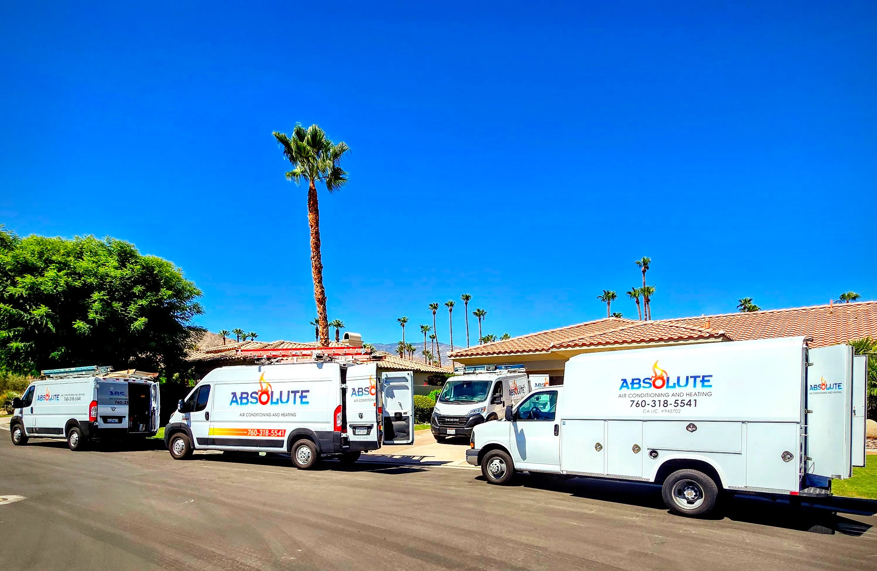Four white Absolute Air Conditioning and Heating service vans parked in a residential area under a clear blue sky with palm trees.