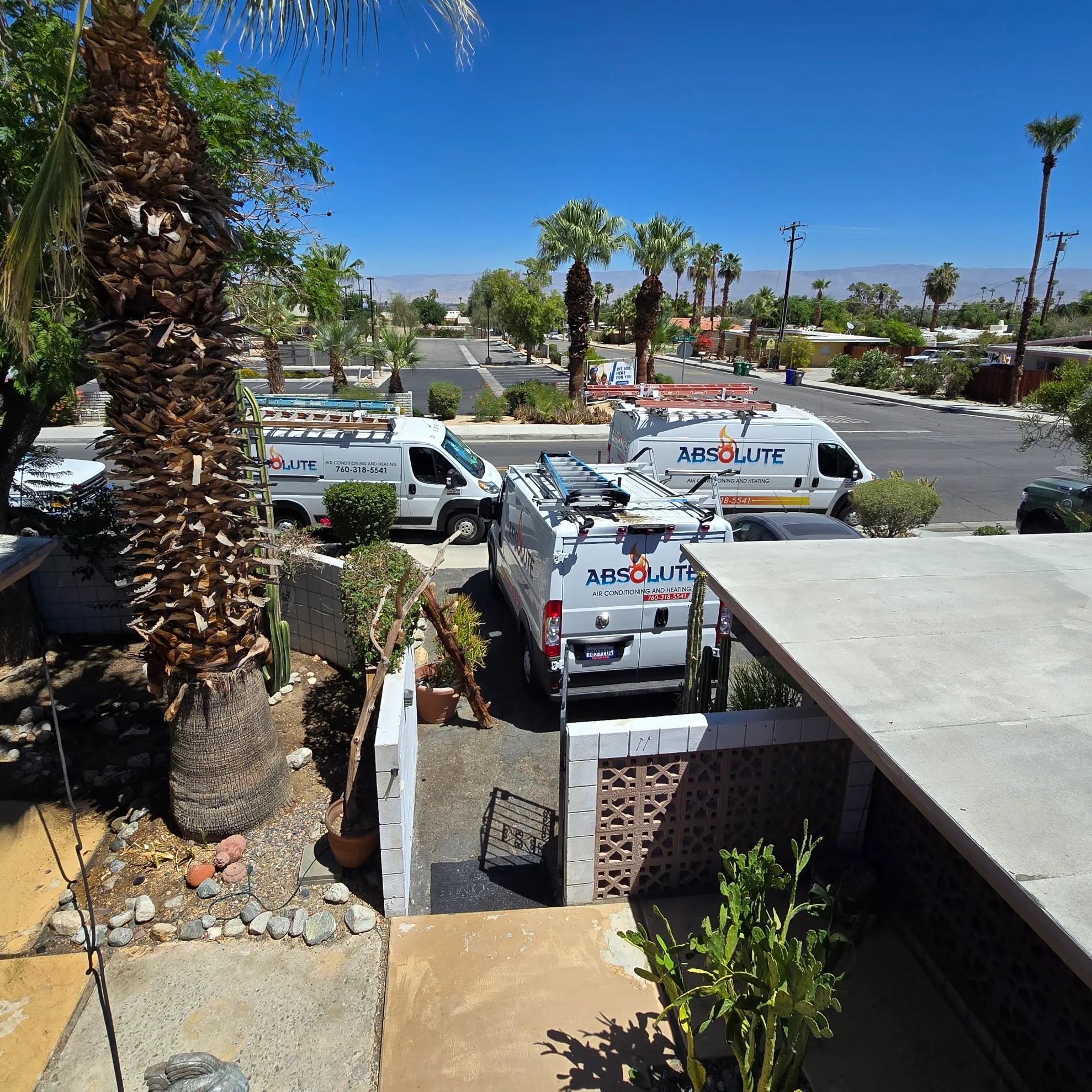 Three white vans from Absolute Air Conditioning and Heating parked in a residential driveway under clear blue sky with palm trees around.