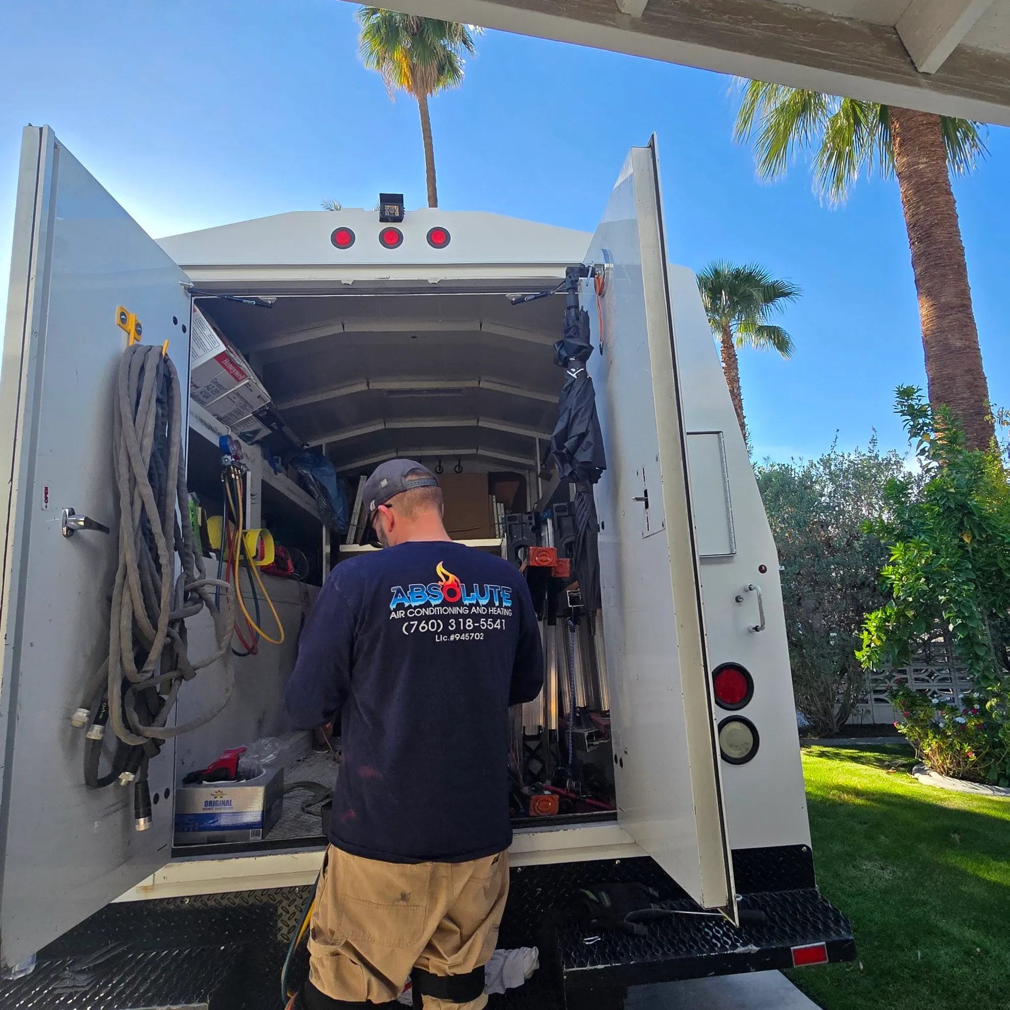 Technician standing at the open back of a service truck with tools and hoses, wearing a shirt with Absolute Air Conditioning and Heating logo.