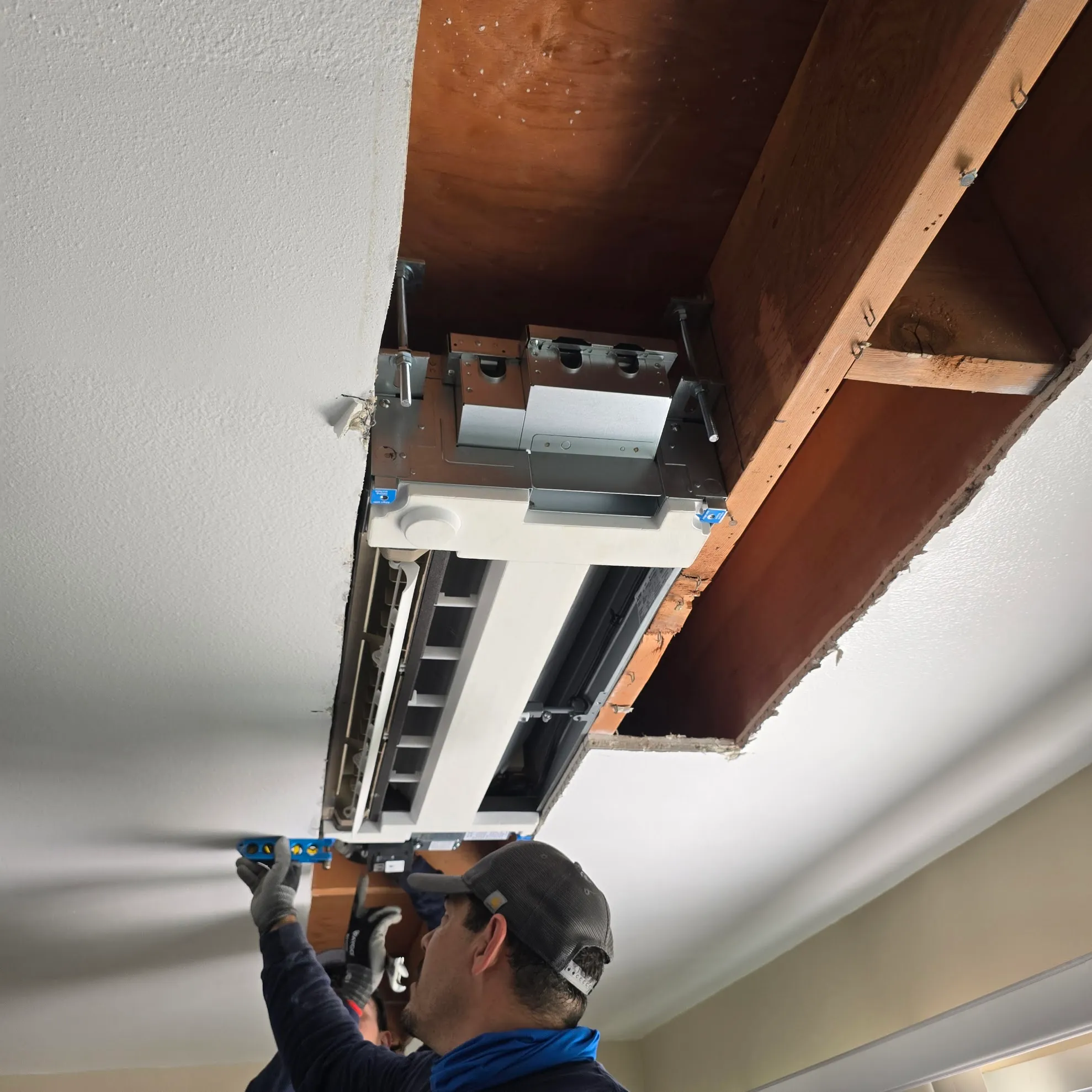 Technician installing a ceiling-mounted cassette air conditioning unit inside a cutout ceiling space.