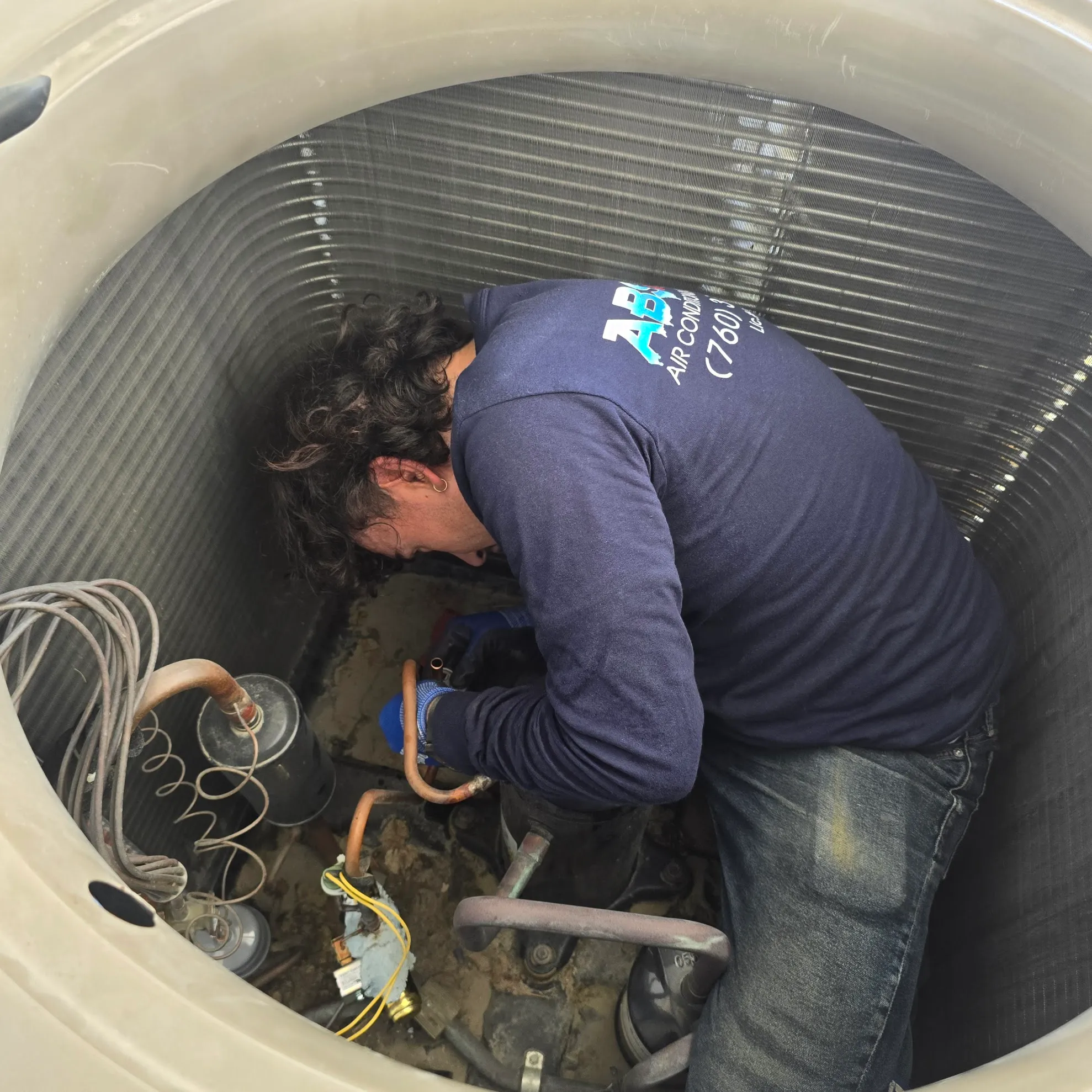 Technician wearing a navy shirt and gloves repairing the inside components of an air conditioning unit.