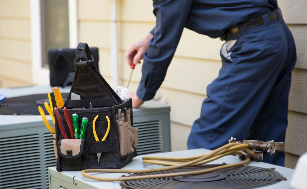 A technician in navy attire repairs an outdoor air conditioning unit.