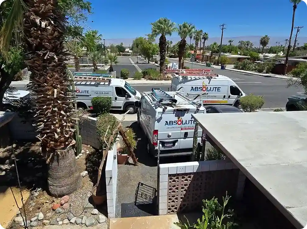 Three white Absolute air conditioning and heating service vans parked near a residential street with palm trees and desert landscaping.