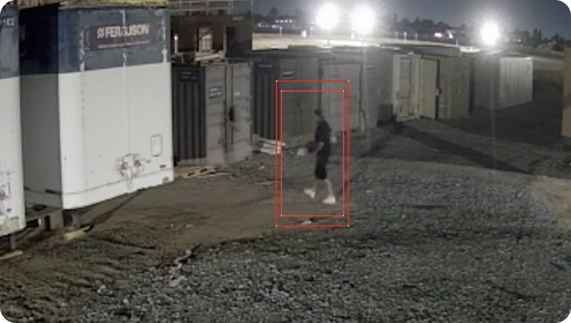 Person trespassing around storage containers at a construction site at night. Red boxes are around the person to show motion tracking.