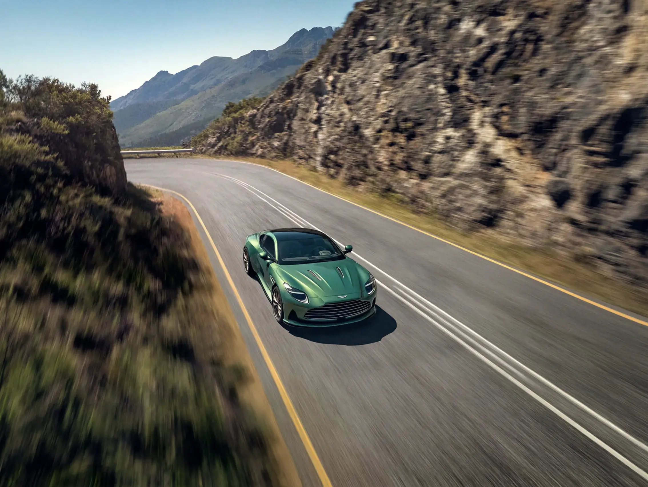 Green Aston Martin coupe driving along a mountain road.