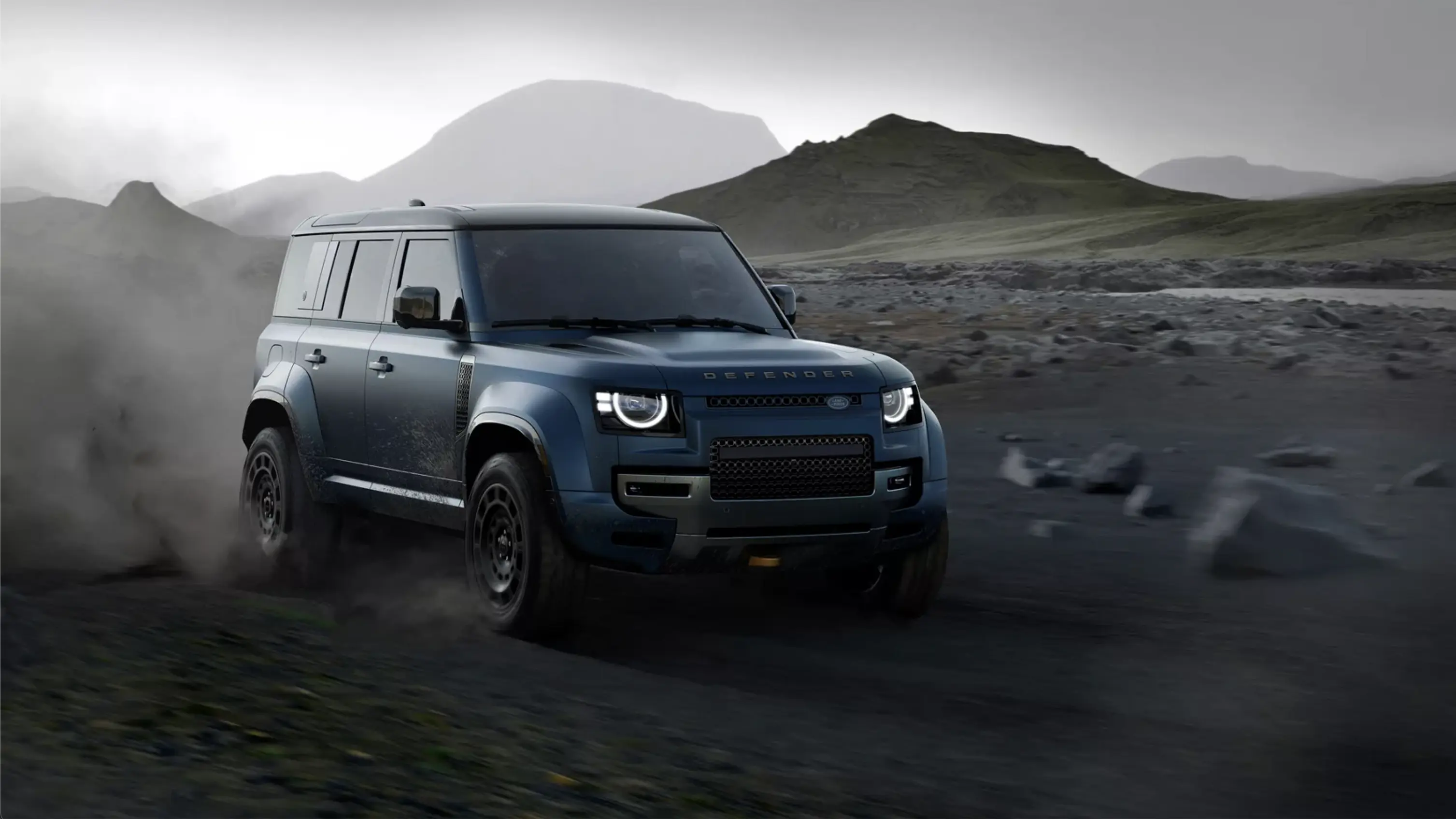Blue Land Rover Defender driving against a rocky mountainous landscape.