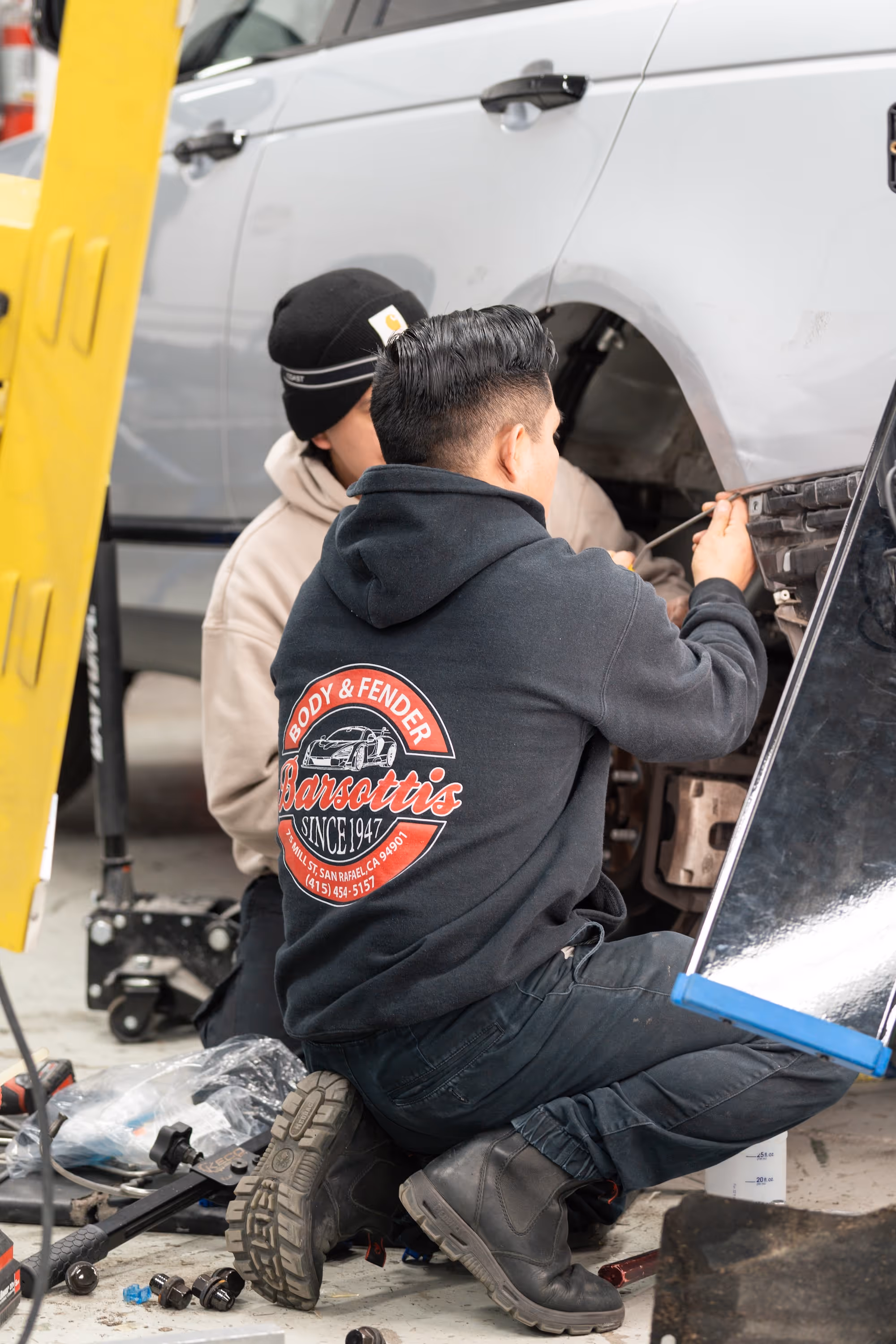 Two Barsotti's Body and Fender collision repair experts working together on a car wheel.