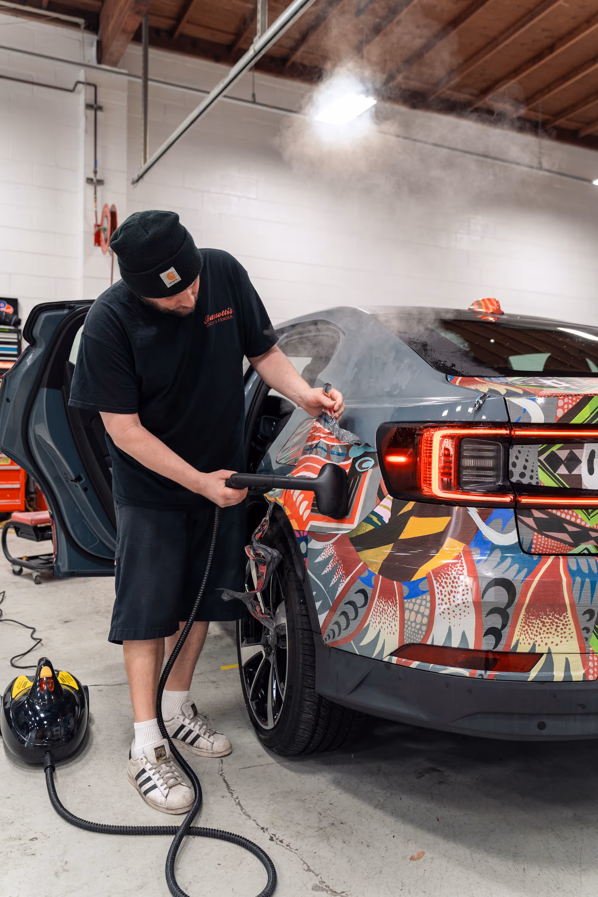 Auto body technician applying a custom wrap to the rear panel of a car.