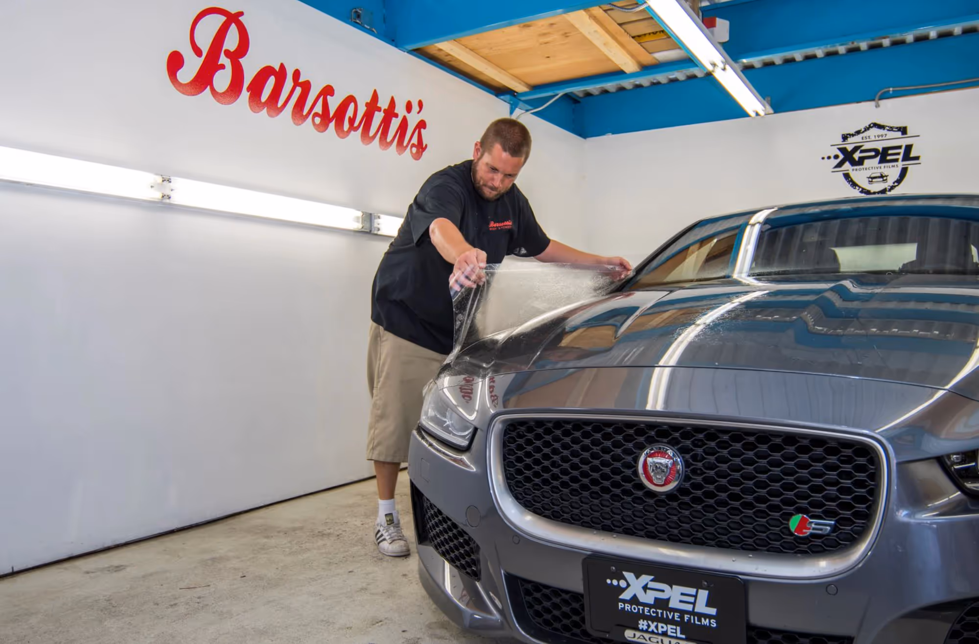 Auto body technician applying paint protecting film to the hood of a Jaguar.