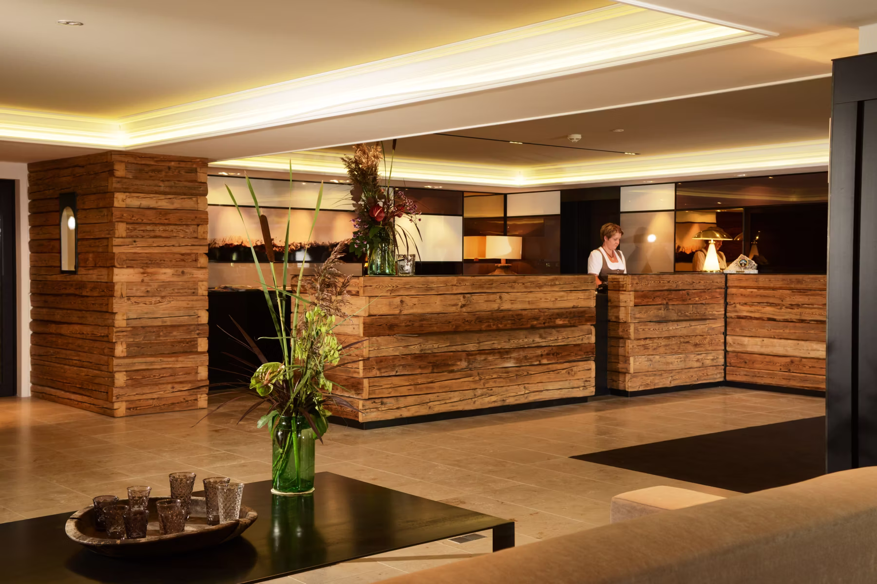 Moderne Hotelrezeption mit rustikalem Holzempfangstresen und einer Mitarbeiterin hinter dem Tresen.