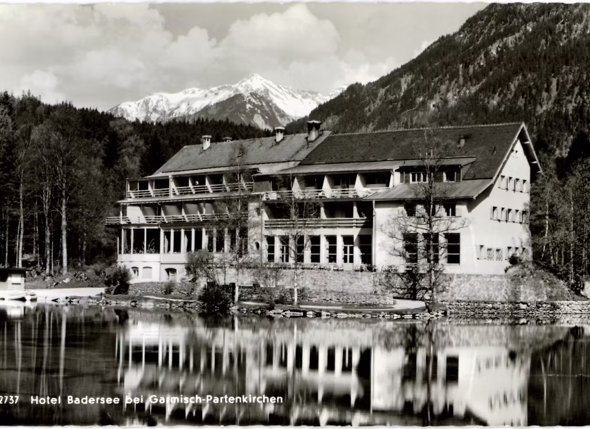 Schwarz-weiß-Foto eines Hotels am Badesee mit Bergpanorama und Spiegelung im Wasser bei Garmisch-Partenkirchen.