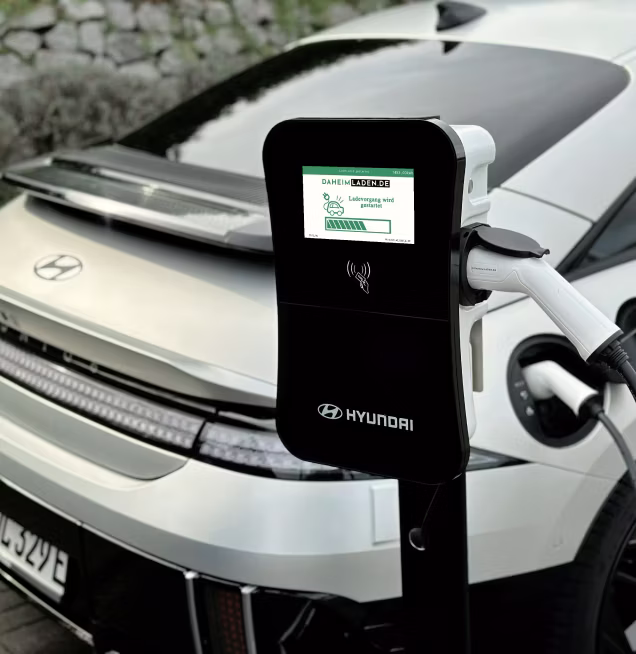 Ein silberner Hyundai Elektroauto, das an einer Hyundai-Ladestation mit Ladekabel verbunden ist.