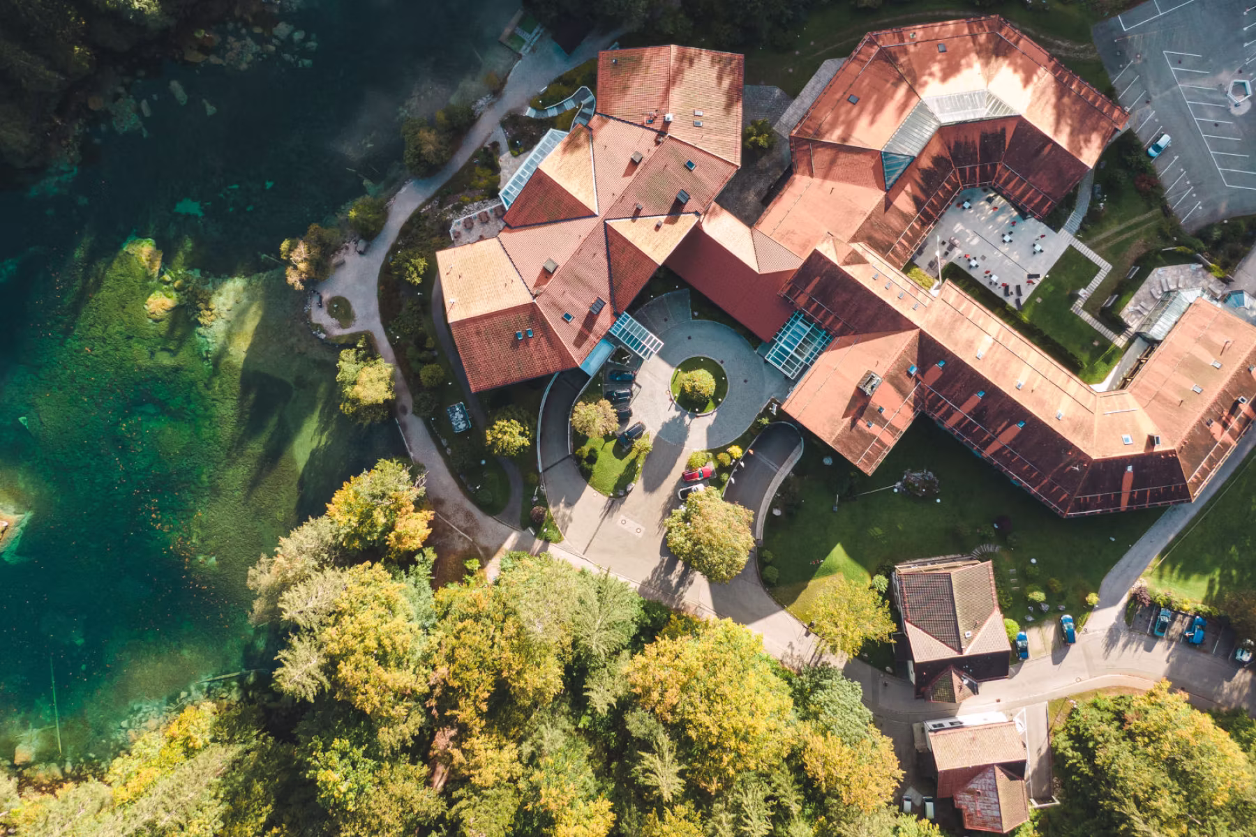 Luftaufnahme von Gebäuden mit roten Dächern neben einem grünen Wald und einem klaren blauen See.
