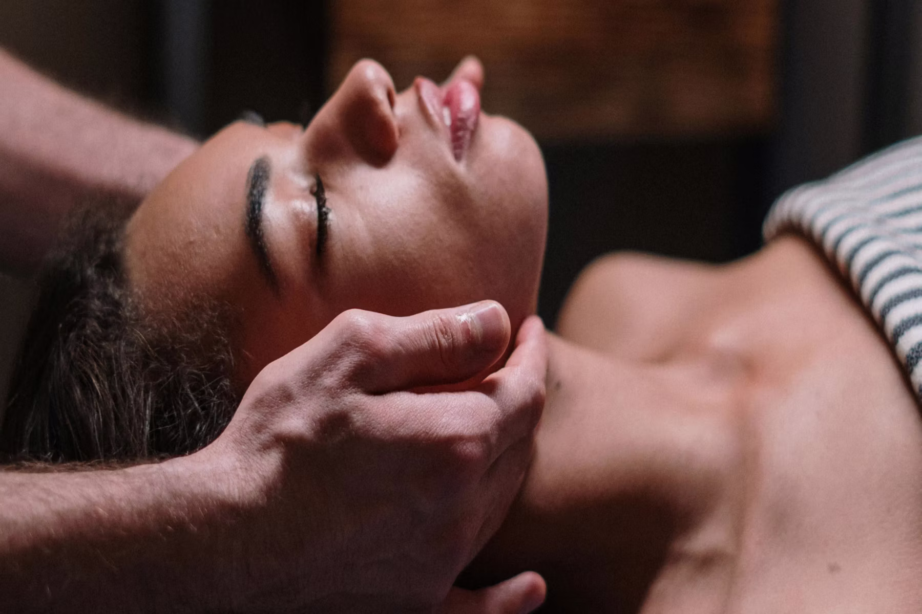 Frau liegt entspannt mit geschlossenen Augen, während Hände sanft ihr Kinn und ihren Kopf halten.