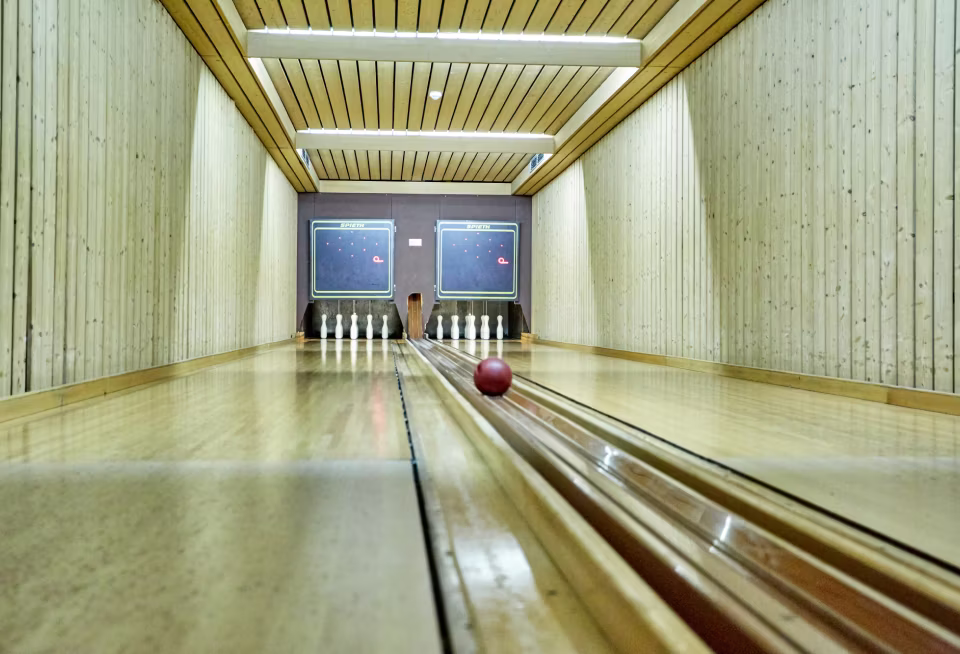 Holzkegelbahn mit zwei Bahnen, ein roter Kegelball rollt auf die weißen Kegel zu.