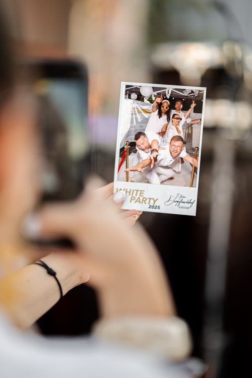 Person holding a photo of five people dressed in white posing playfully at a 2025 White Party event.