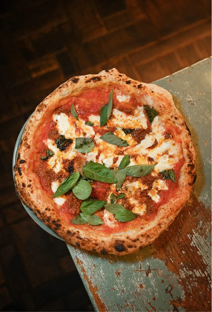 Pizza napolitaine avec sauce tomate, mozzarella fondue et feuilles de basilic fraîches sur une table en bois usée.