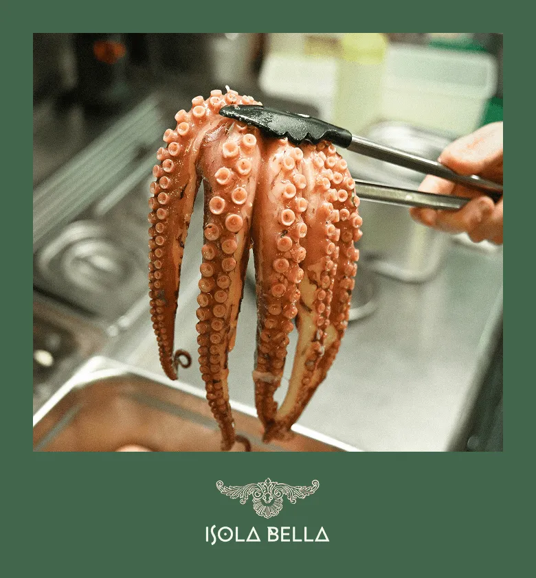 Main tenant des pinces saisissant un gros tentacule de poulpe cuit dans une cuisine professionnelle.