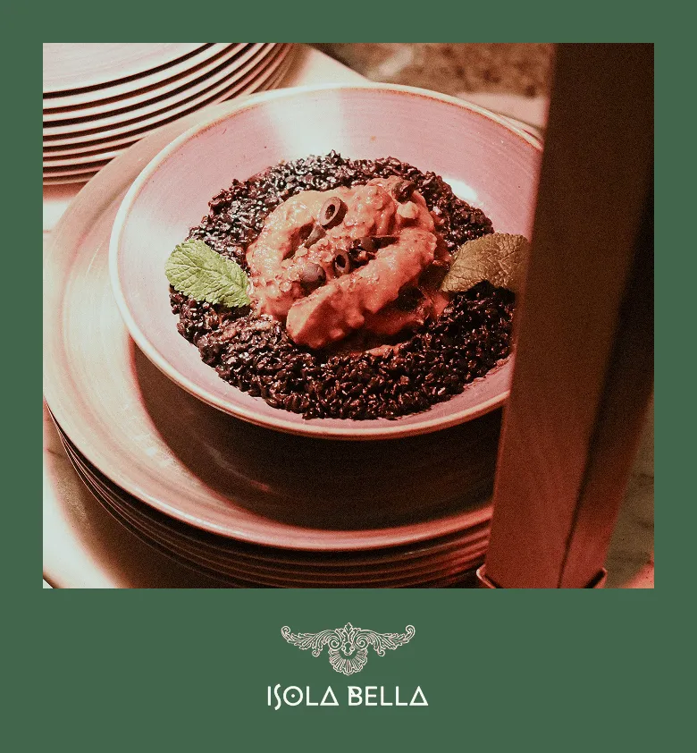 Assiette de riz noir avec une garniture crémeuse et olives noires, décorée de feuilles de menthe.