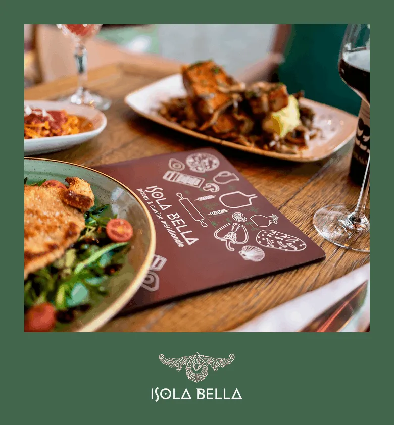 Table en bois avec plats italiens, menu Isola Bella et verre de vin rouge.