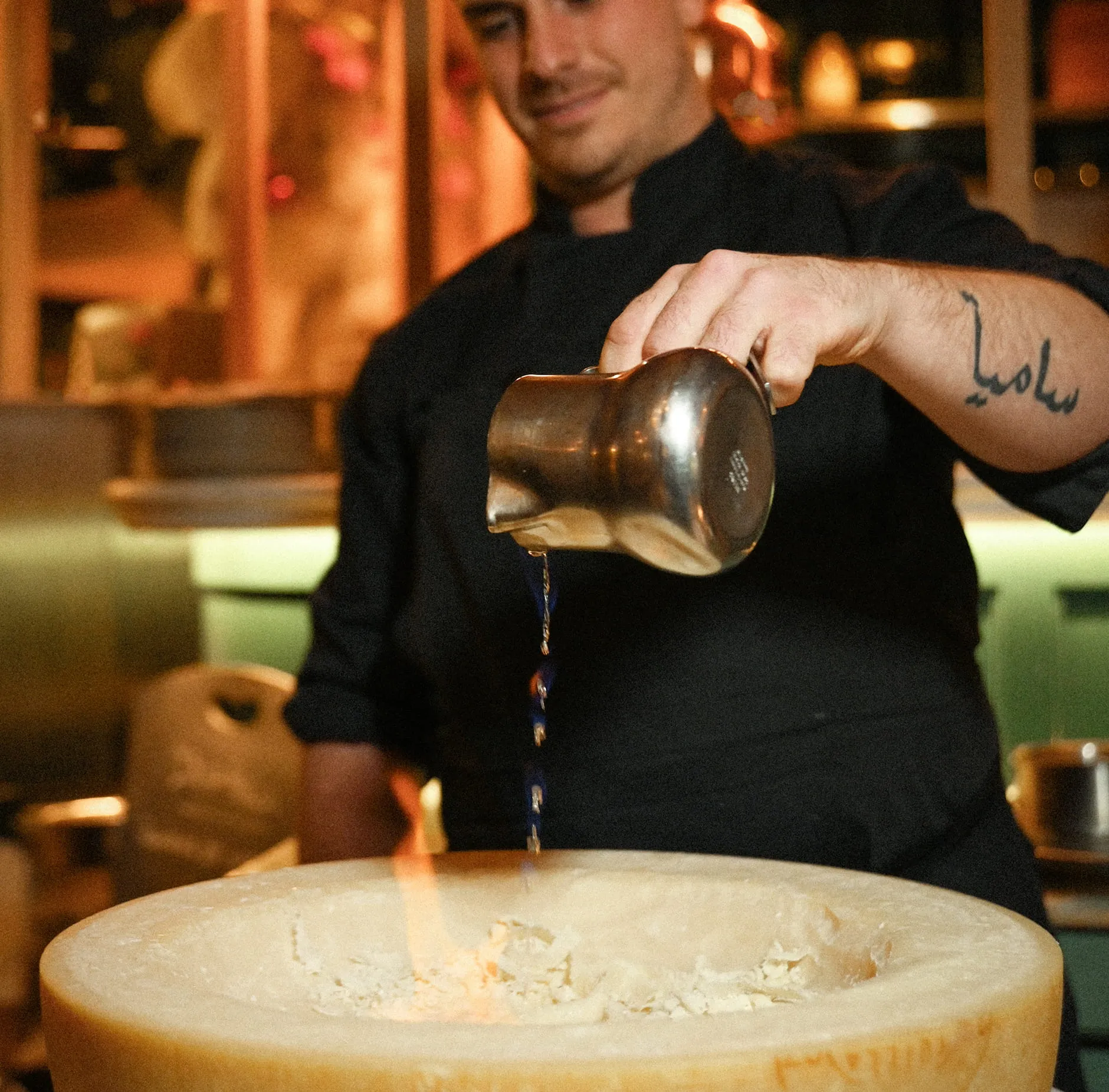 Un chef verse un liquide depuis un pot en métal dans un grand fromage creusé.