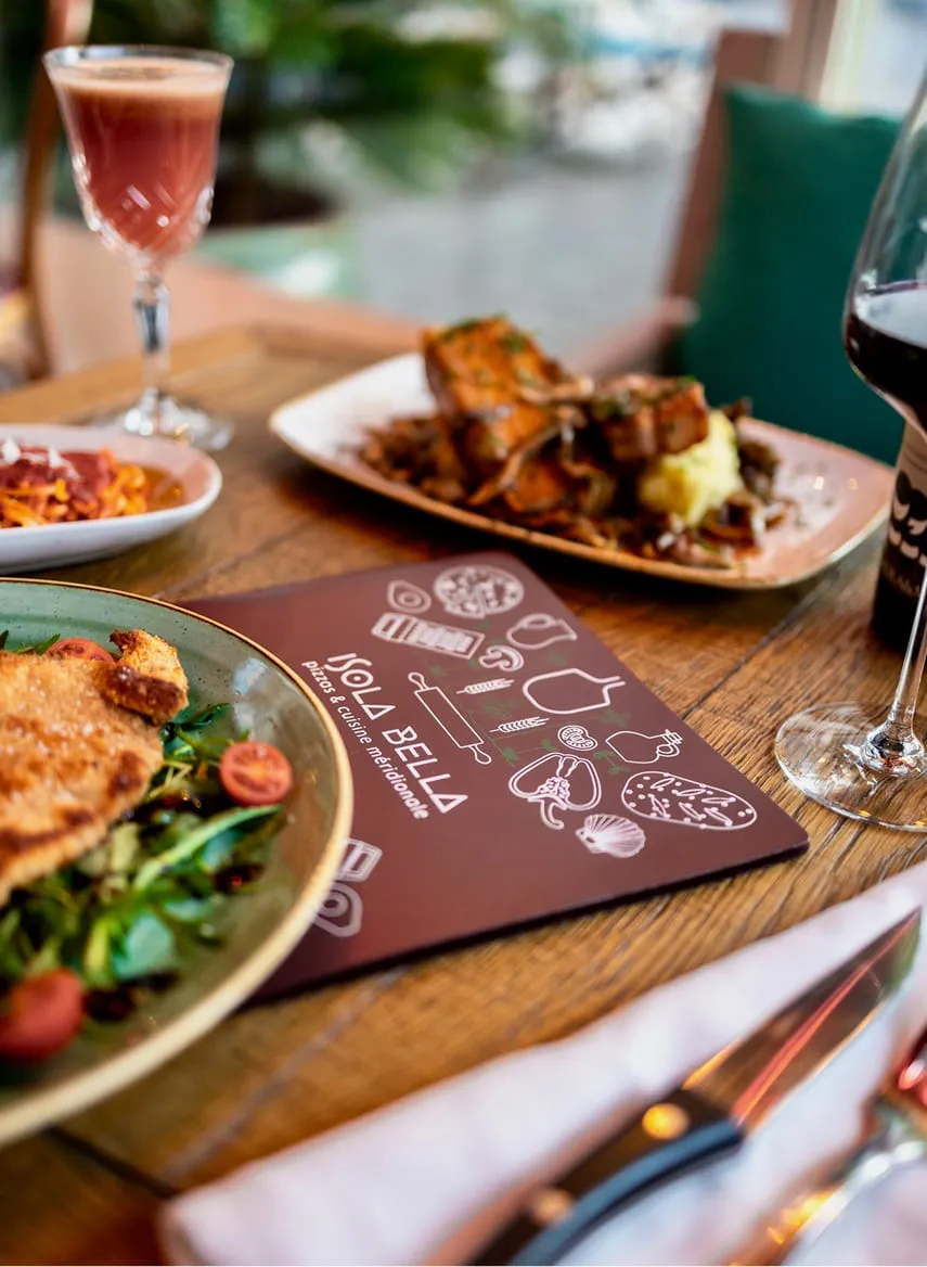 Table avec plusieurs plats préparés, un verre de vin rouge, un verre de cocktail rosé, et un menu du restaurant Isola Bella.