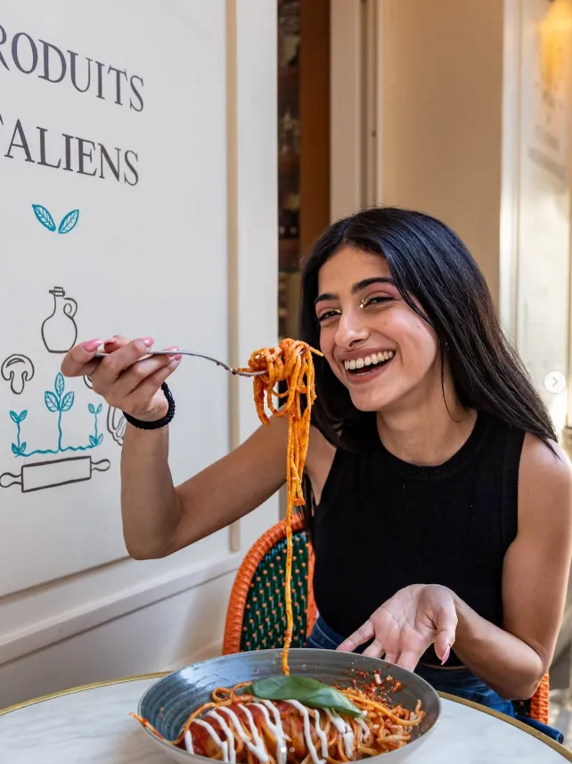 Jeune femme souriante portant un haut noir, mangeant des spaghettis à la sauce tomate assis dans un café.