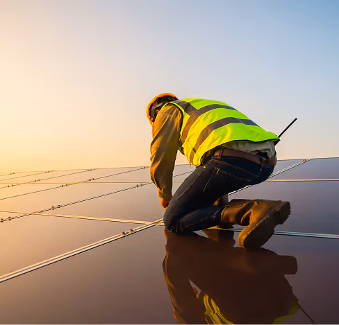 Worker in a safety vest and helmet installing or inspecting solar panels at sunset