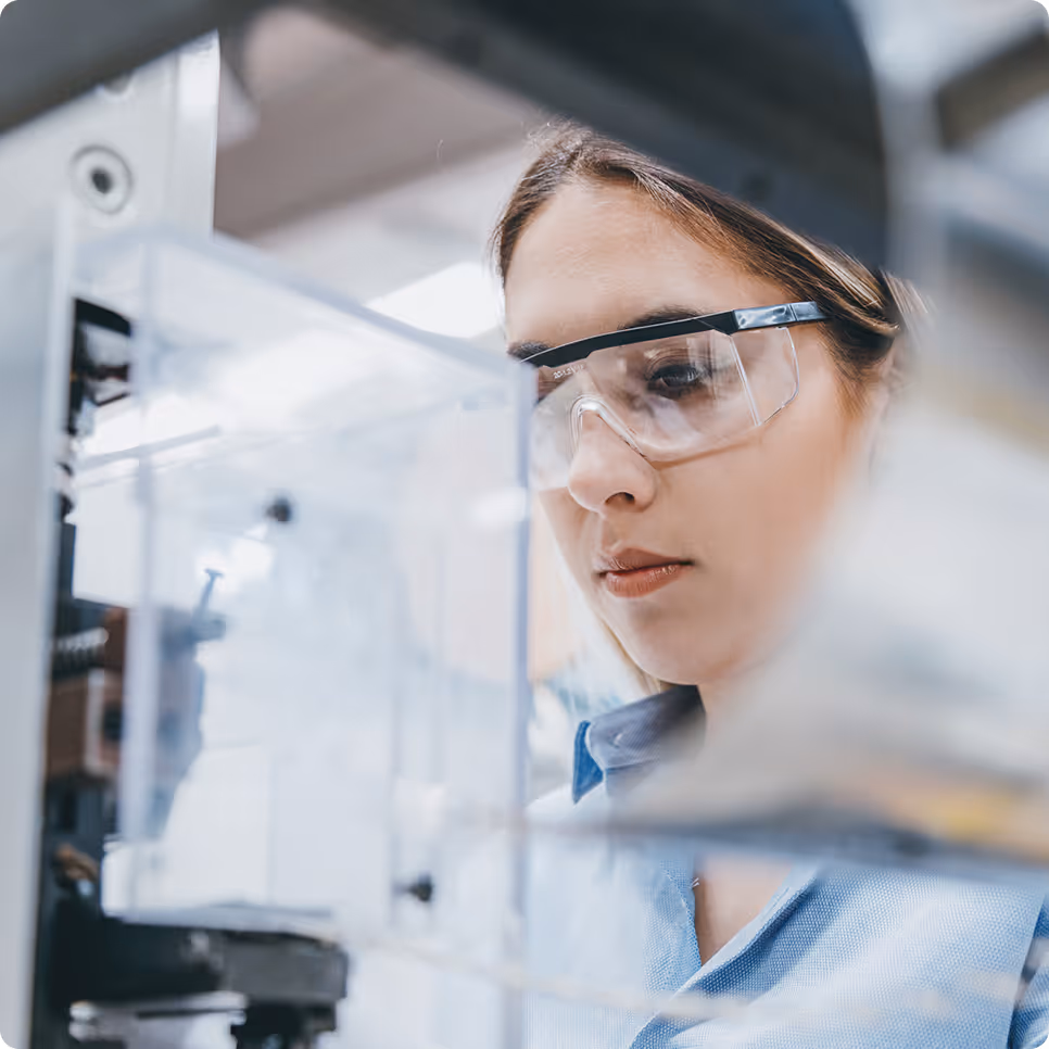 Woman wearing safety goggles closely inspecting industrial machinery