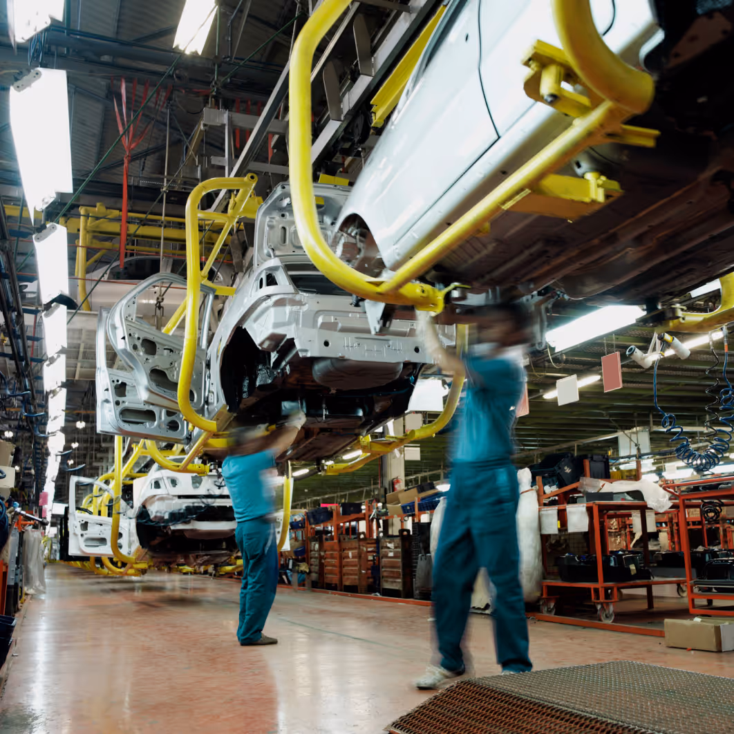 Workers assembling white car frames on a conveyor system in an automotive factory