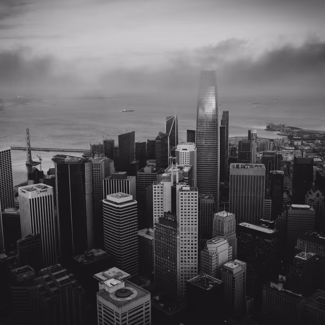 Black and white aerial view of a dense city skyline with tall skyscrapers near a large body of water and a bridge