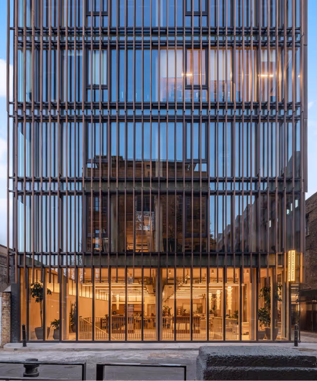 Modern glass building facade with vertical metal bars and illuminated interior at dusk