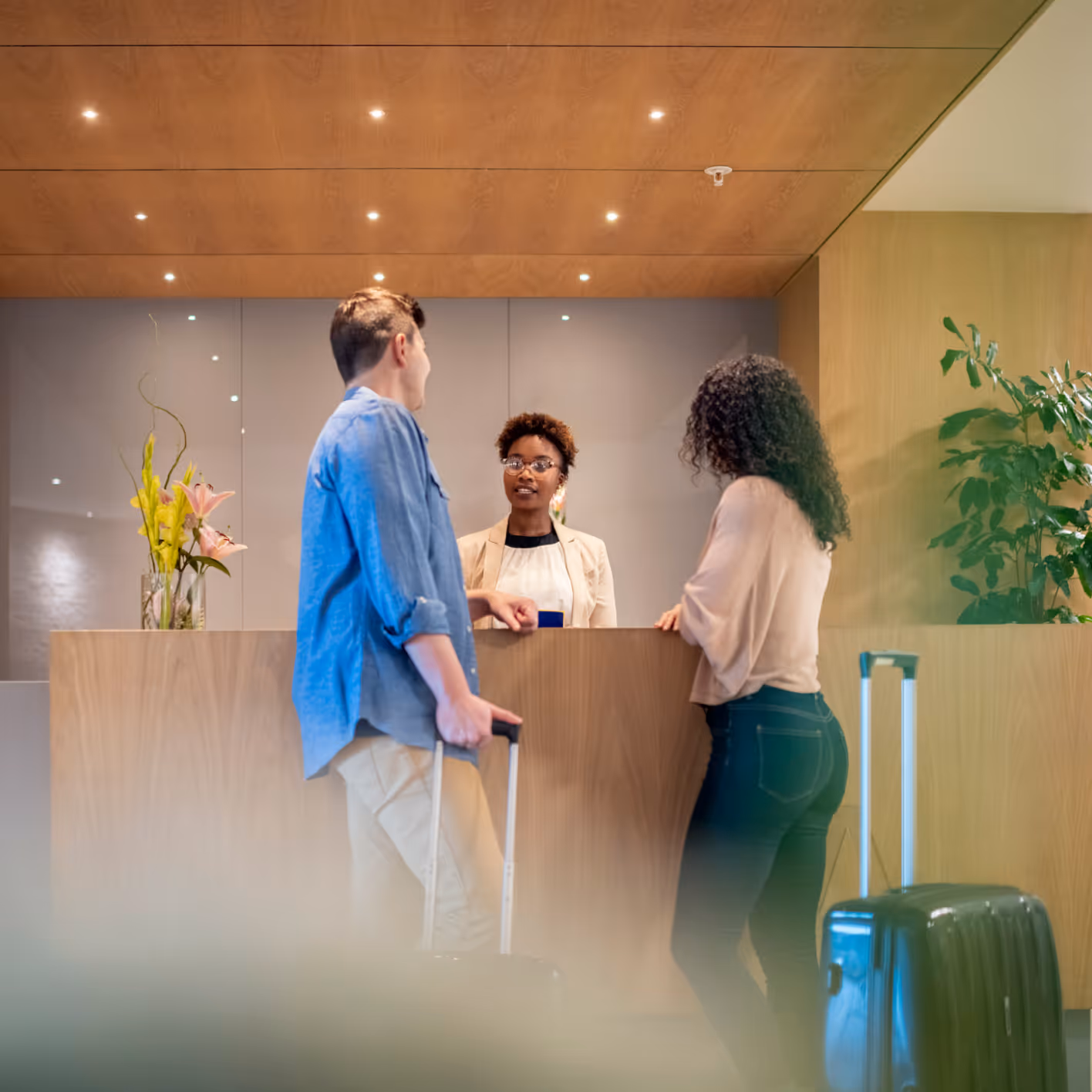 Couple with suitcases talking to a receptionist at a hotel front desk