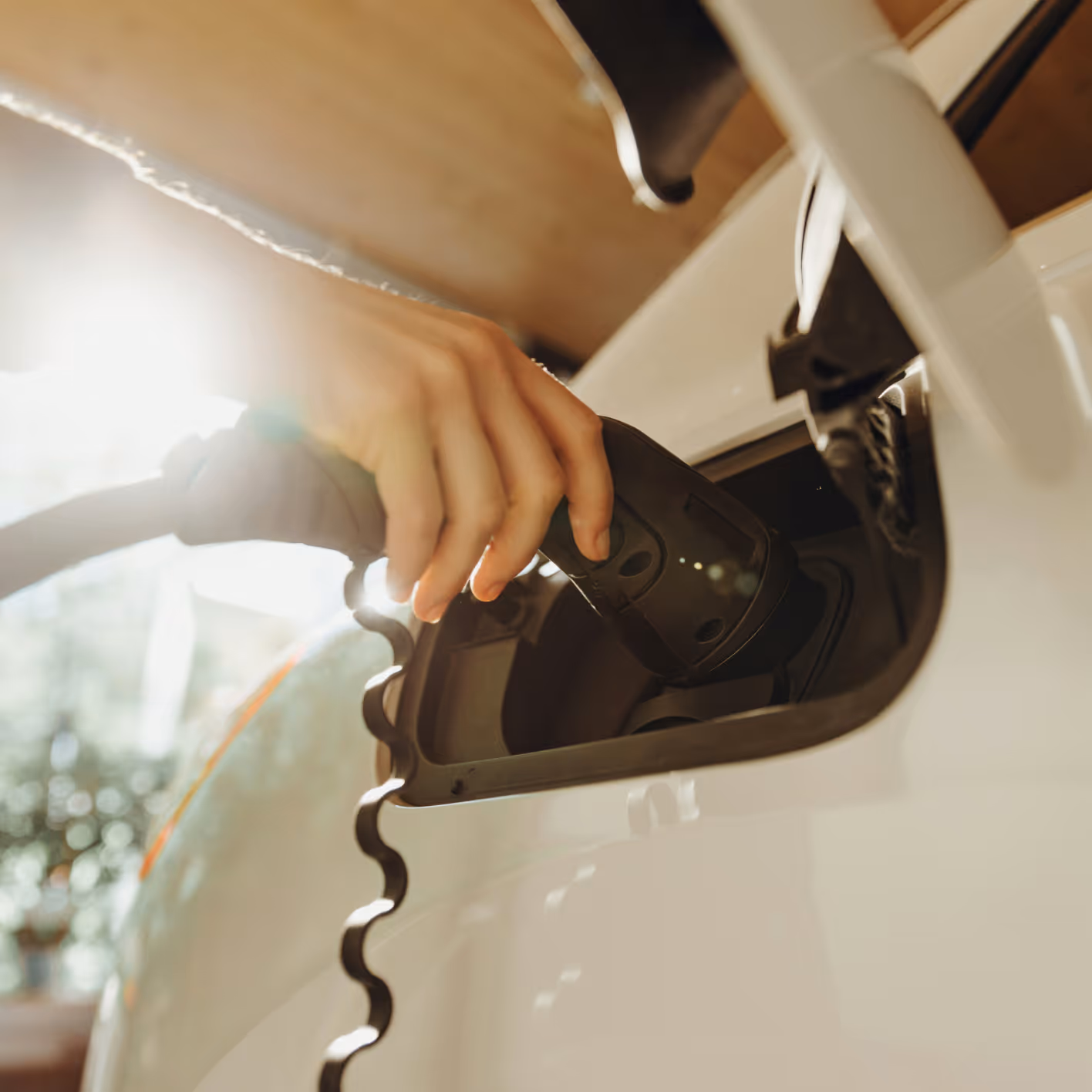 Hand plugging an electric vehicle charging connector into a white car