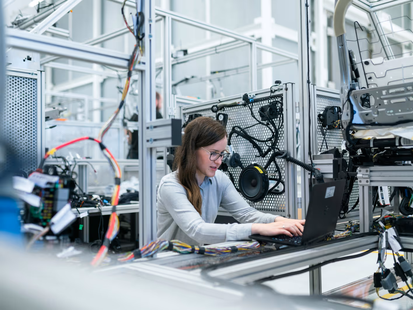 Woman working on a laptop in a high-tech lab surrounded by automotive electronic components and wiring