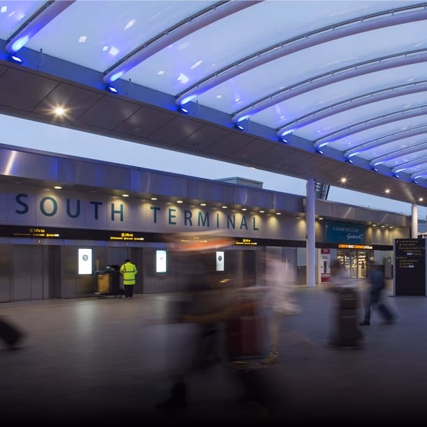Exterior view of an airport Terminal with a modern curved roof and blurred travelers walking by with luggage for London Gatwick brand