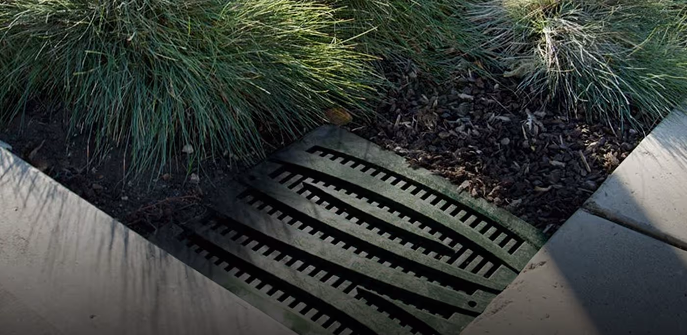 Rectangular metal storm drain grate surrounded by green grass and concrete sidewalk edges for NDS brand