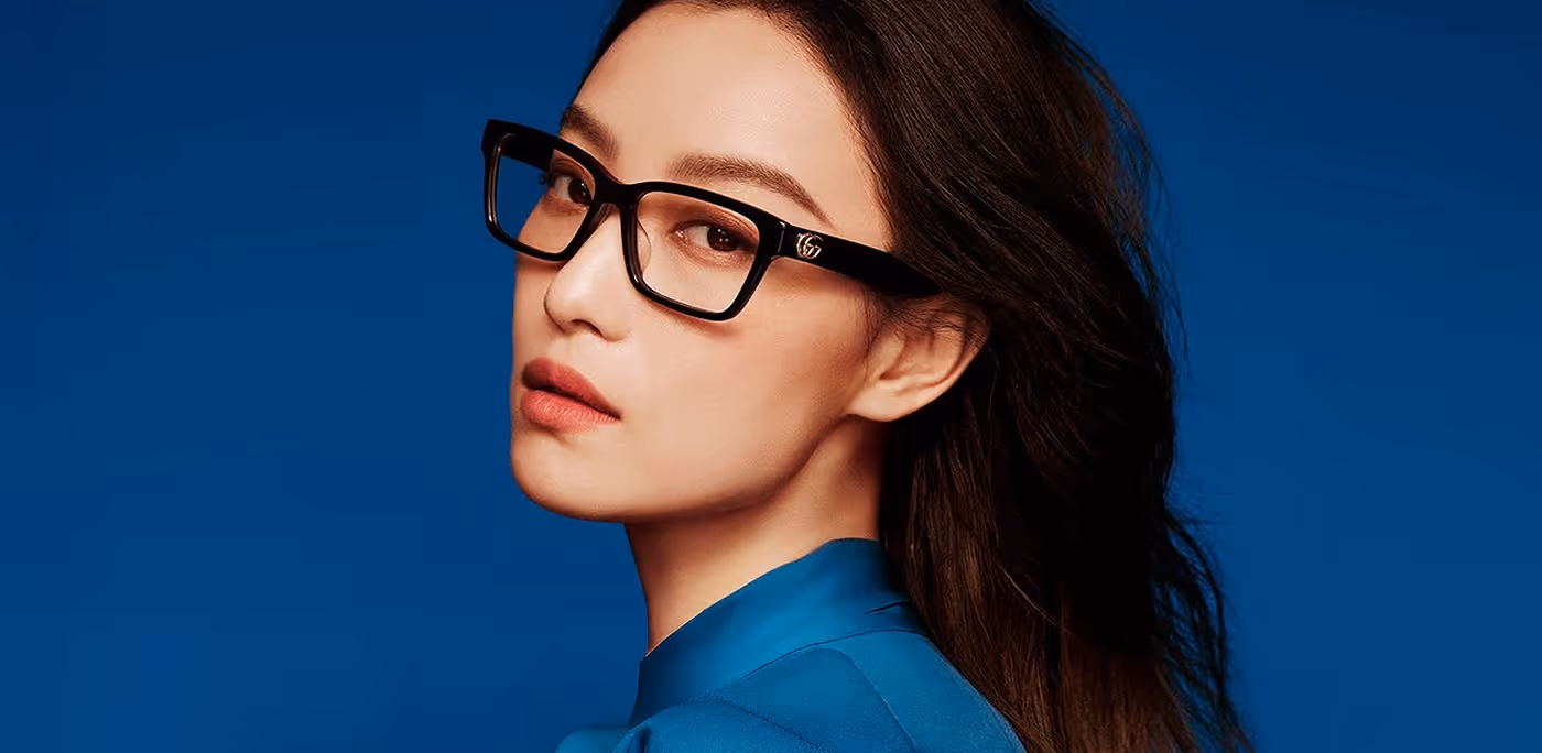 Portrait of a woman wearing black glasses and a blue top against a dark blue background for Boots Opticians brand