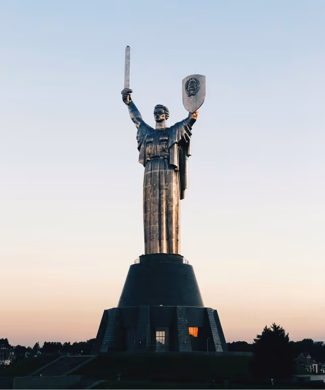 The Motherland Monument in Kyiv, Ukraine, holding a sword and shield against a clear sky at dusk